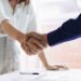 Two people shaking hands over a table.